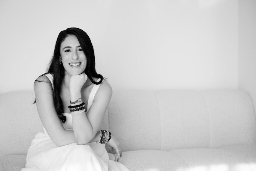 JodiPlumbley_Simmone-44_websize Black and white photo of Simmone Helander seated on a couch, chin on fist, smiling