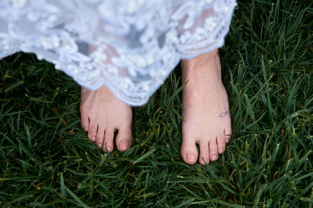 Bare feet standing in green grass beneath a white lace dress
