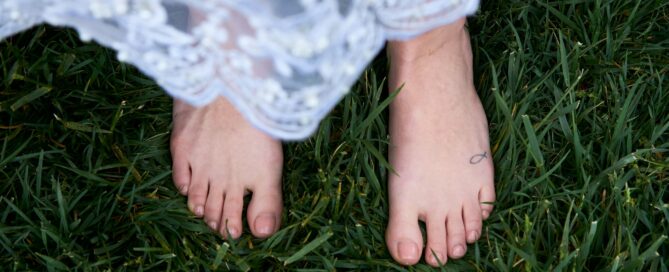 Bare feet standing in green grass beneath a white lace dress