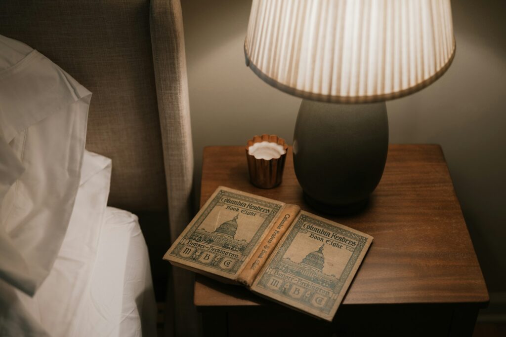 Soft bedside lamp glowing beside an open book and candle at night