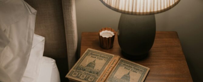 Soft bedside lamp glowing beside an open book and candle at night